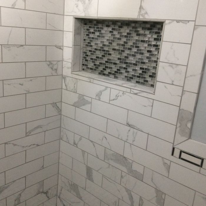 Shower wall with white marble-look subway tiles and a recessed niche featuring a decorative gray and white mosaic tile.