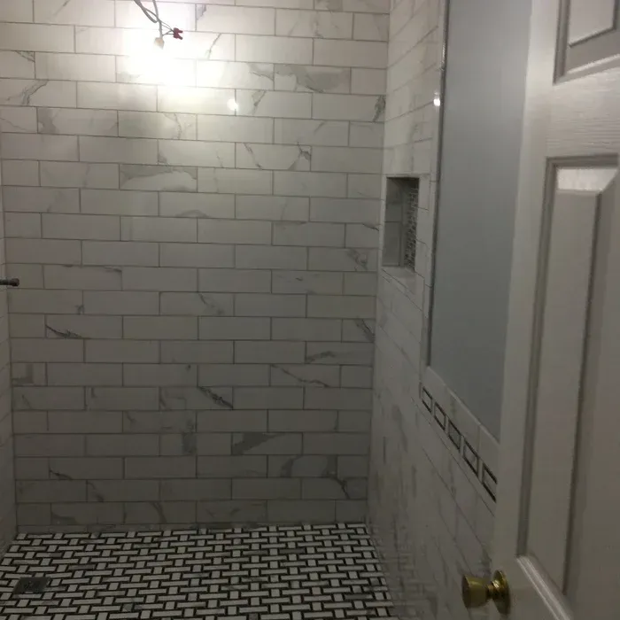 A tiled shower enclosure with white marble subway tiles on the walls and a black and white basketweave floor pattern.