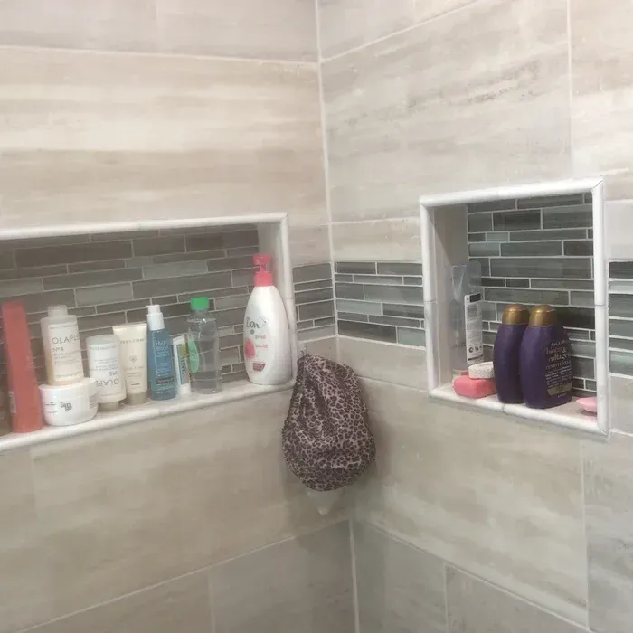 Two tiled shower niches with shelves containing various shampoo, conditioner, and soap bottles, plus a hanging shower cap.