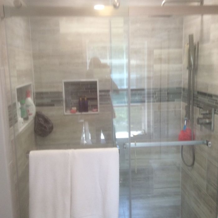 A modern walk-in shower with light wood-look tile, a glass door, two inset wall niches, and a white towel hanging on it.