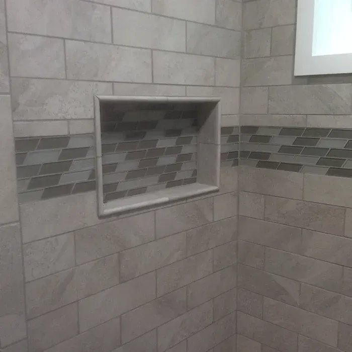A rectangular recessed shower niche framed by light tiles with a dark, horizontally-patterned mosaic tile accent strip.