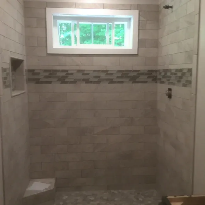 A walk-in shower with neutral-toned rectangular wall tiles, a mosaic accent strip, a small window, and a built-in seat.
