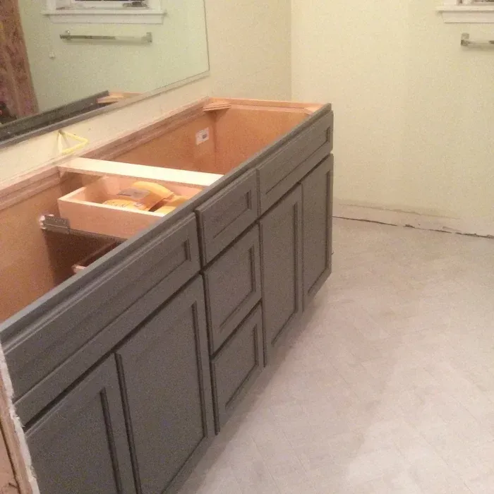 A gray bathroom vanity cabinet with an open drawer and unfinished top installed against a wall with a mirror above.