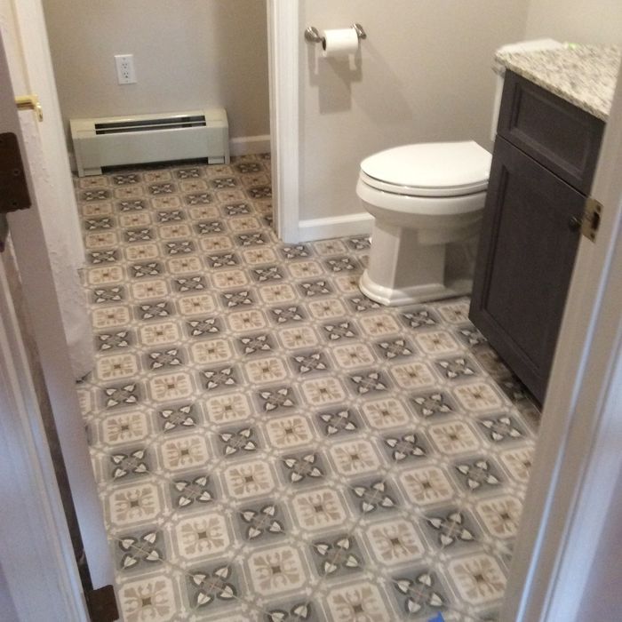 A small bathroom with a patterned tile floor, a white toilet, and a dark grey vanity cabinet.