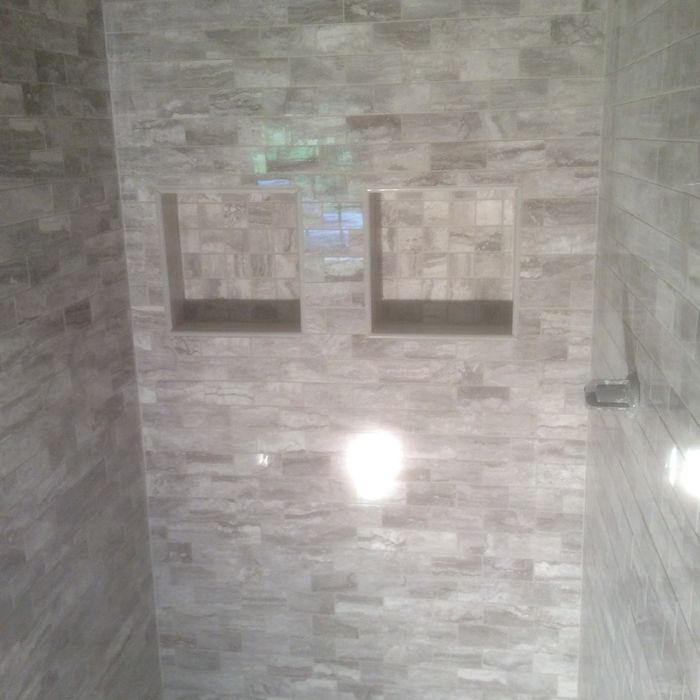 A shower wall covered in gray, stacked stone-style tile with two built-in square recessed storage niches.