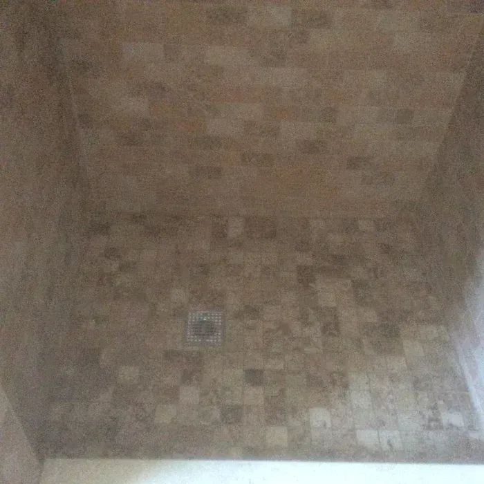 A shower stall featuring square-patterned, earth-toned stone tiles on the floor and walls with a central drain.