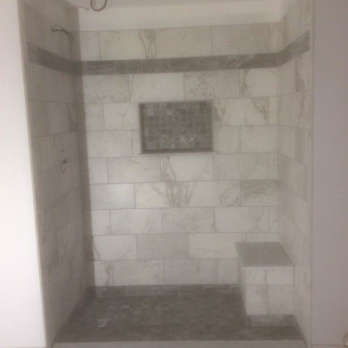 A walk-in shower with white marbled wall tiles, a grey mosaic accent stripe and niche, and a tiled built-in seat.