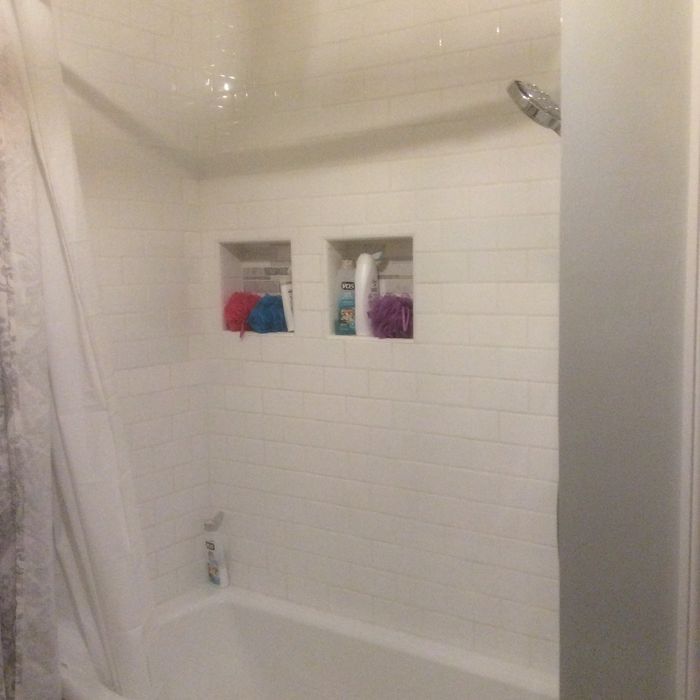 A white tiled shower enclosure with two recessed shelving niches containing toiletries and bath sponges.