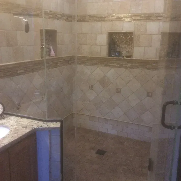 A walk-in shower with beige, diamond-patterned tile walls, decorative horizontal stone accents, and built-in niches.