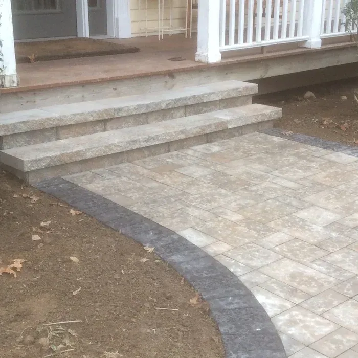 Stone steps leading up to a porch, bordered by a curved path of light pavers with a dark gray cobblestone edge.