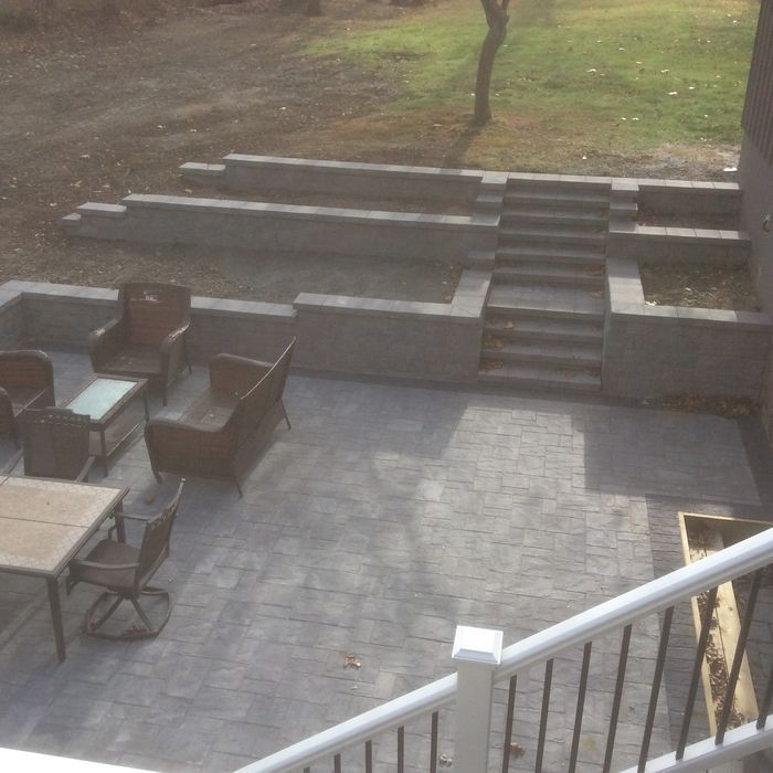 A multi-level patio with stone pavers, outdoor furniture, and a set of tiered stone steps leading to a grassy lawn.