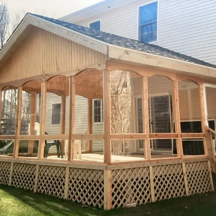 A newly built wooden deck with a screened-in porch, vaulted roof, and lattice skirting, attached to a house.
