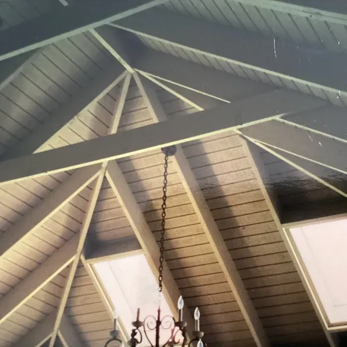 A vaulted ceiling with exposed wooden rafters and planking, featuring a central chandelier and recessed skylights.