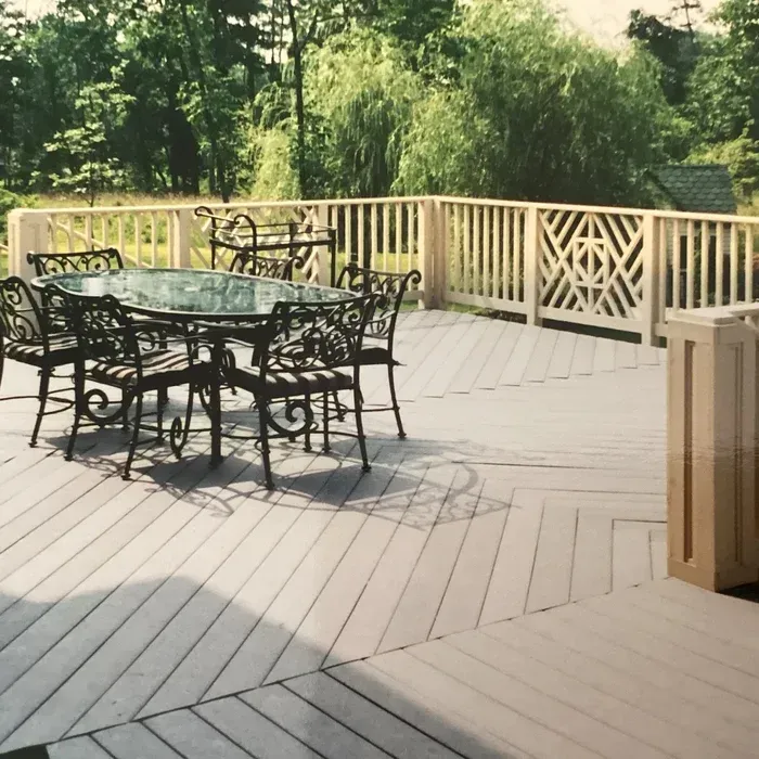 A light grey deck with a herringbone-patterned floor, a wrought iron dining set, and decorative wooden railing.