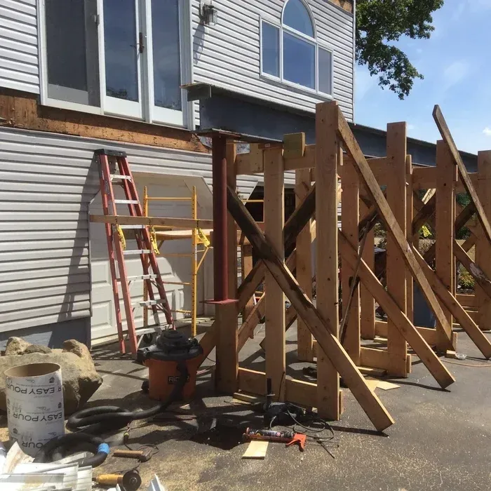 A wooden temporary support structure holds up a steel beam under the exterior wall of a white house being renovated.