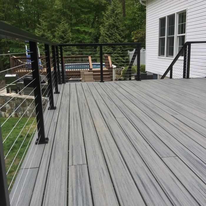 A gray composite deck with a black metal railing and cable infill system, looking out toward a backyard and pool.
