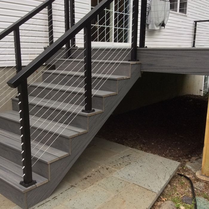Outdoor gray composite deck stairs with black railings and horizontal cable balusters, leading to a home’s sliding door.
