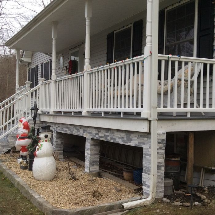 A porch decorated for Christmas with a Santa figure and a snowman on the gravel ground below.