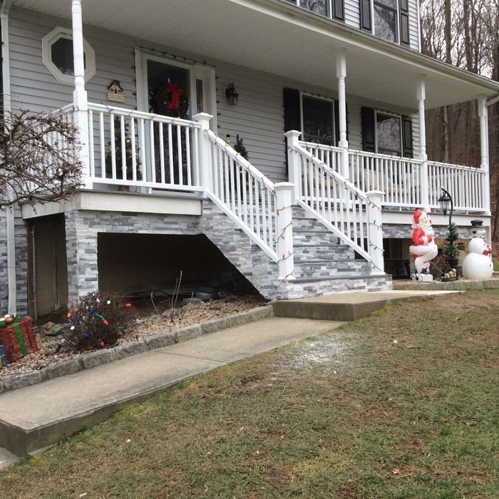 A light gray house with a stone-covered foundation and a white porch, decorated for Christmas with a Santa and snowman.