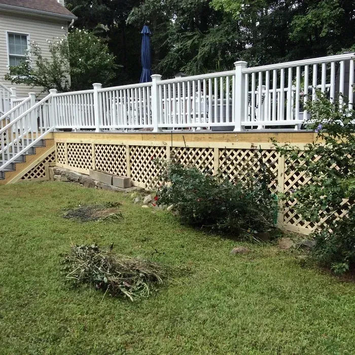A white deck railing above a wooden lattice skirting, with wooden stairs and a grassy backyard area in the foreground.