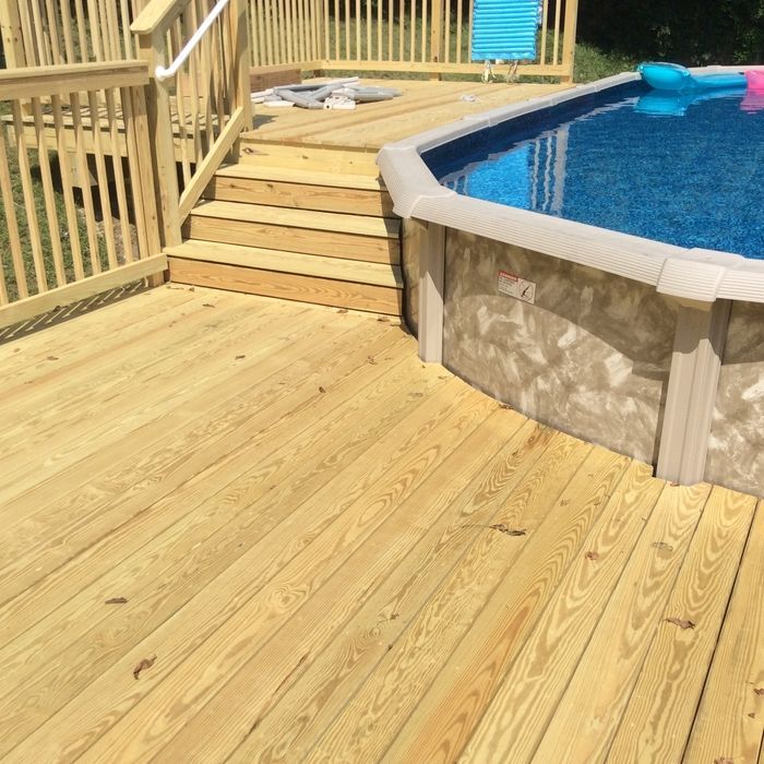 Wooden deck with stairs leading up to an above-ground swimming pool with blue water.