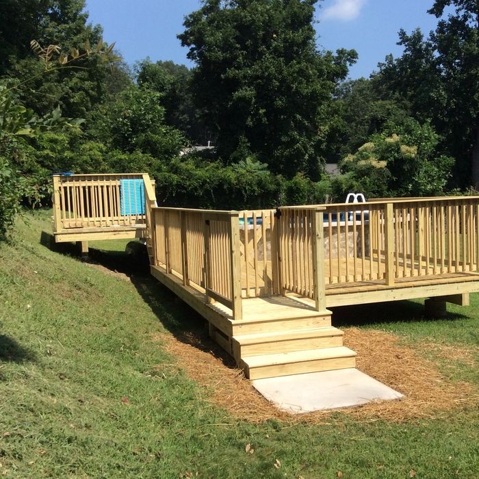 A multi-level wooden deck with safety railings and stairs leading to a swimming pool in a grassy backyard.