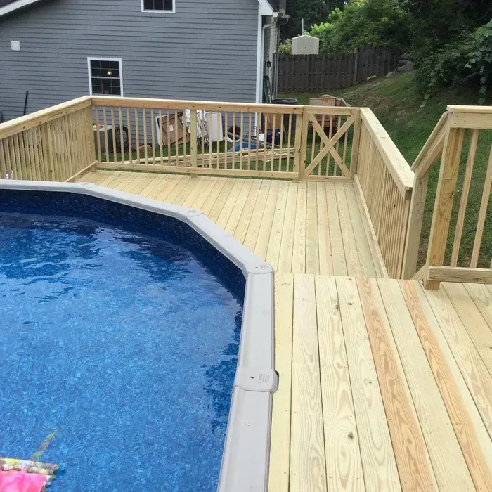 A newly constructed wooden deck built around a circular above-ground swimming pool, with a gate and stairs leading down.