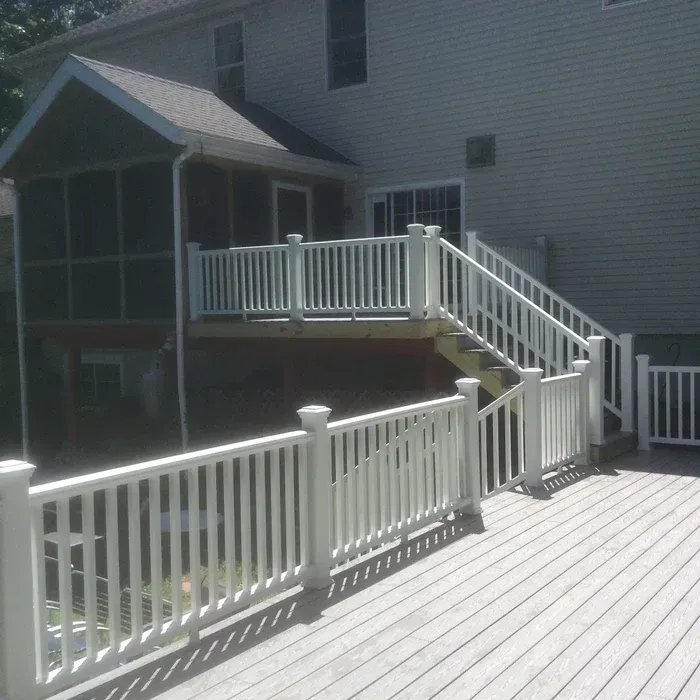 A gray composite deck with white railings, featuring a staircase leading up to an attached screened-in porch.