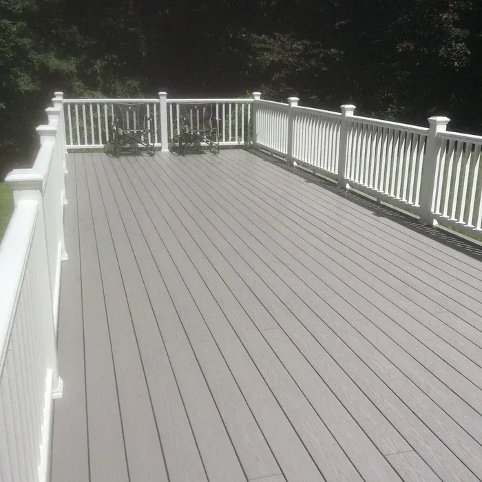 A light gray composite deck with white railings and two chairs, extending toward a dark treeline.