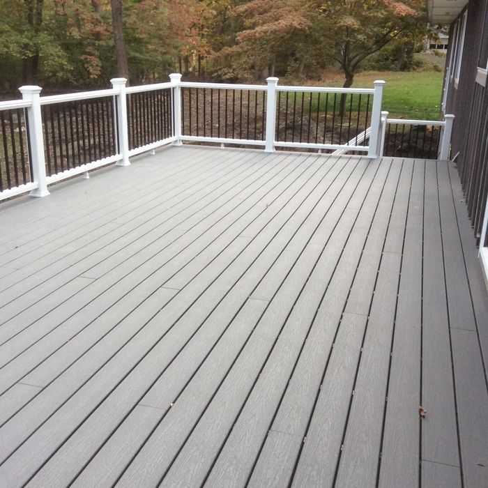 A spacious, modern grey composite deck with a white railing and dark balusters, overlooking a wooded yard in autumn.