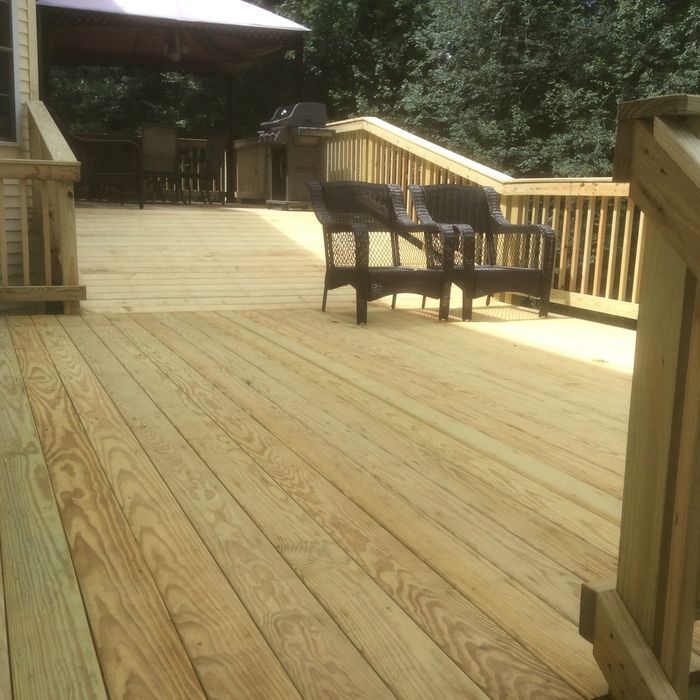 A wooden deck with a set of stairs leading to an upper level, featuring two dark chairs and a grill in the background.
