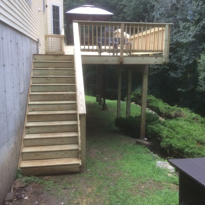A wooden deck with a staircase leading down to a grassy yard next to the side of a house.
