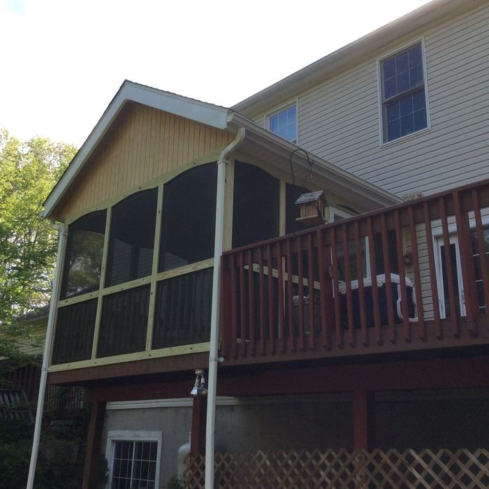 A yellow screened-in porch addition attached to the side of a multi-story house with a wooden deck and lattice skirting.