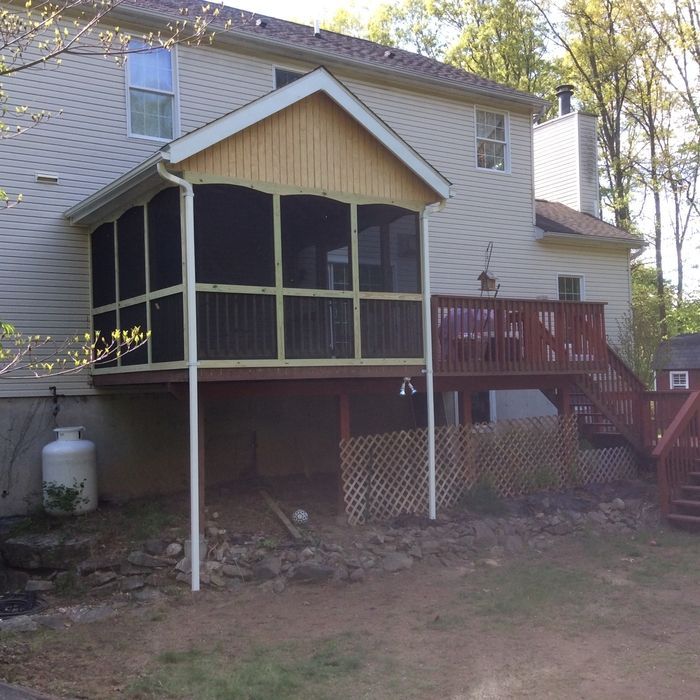 A light-sided two-story house with a screened-in porch and an adjacent wooden deck with stairs leading to the yard.