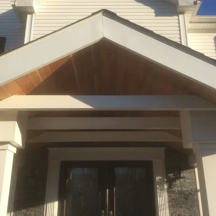 A white-trimmed front entrance porch with a cedar wood-paneled gable ceiling over dark double doors.