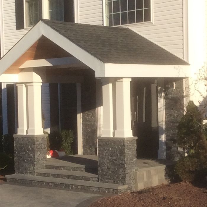 A modern home entrance with a gabled roof, white pillars, stone bases, and concrete steps leading to the front door.