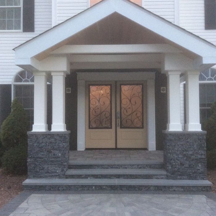 The front entrance of a house featuring a white portico, stone-based pillars, double glass doors, and stone steps.