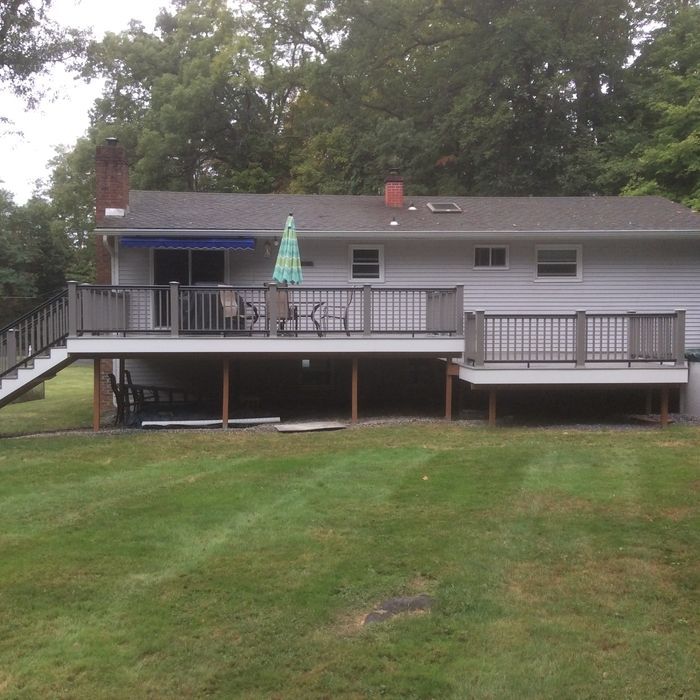 A light gray house with a two-tiered deck, dark railings, and a small staircase in a grassy backyard.