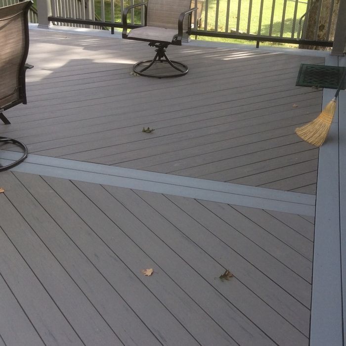A gray deck with a diagonal pattern and a single border board, featuring a patio chair and a broom propped against a post.