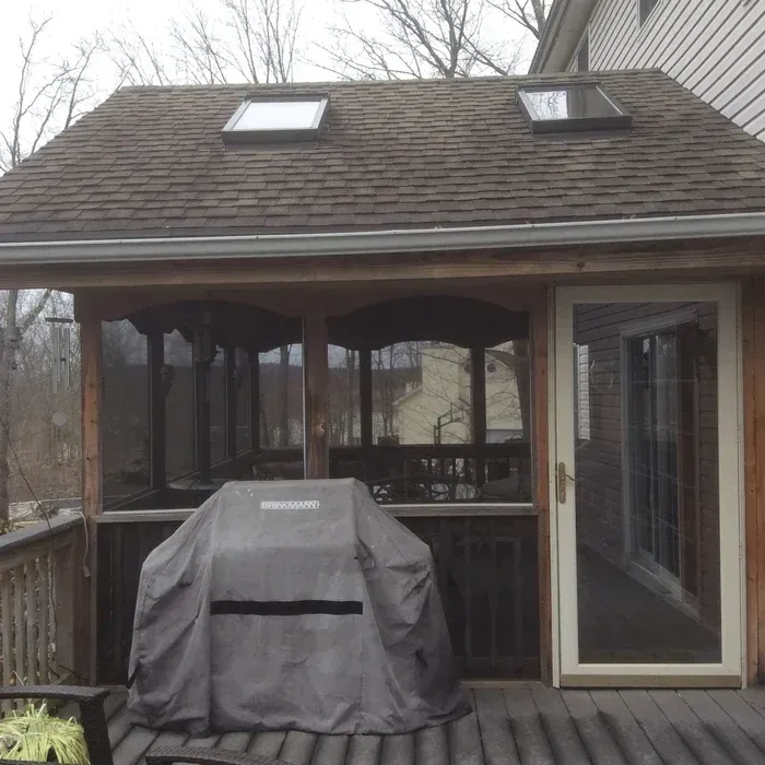 A covered outdoor deck featuring a grill with a gray cover, a screen enclosure, and two skylights on the roof.