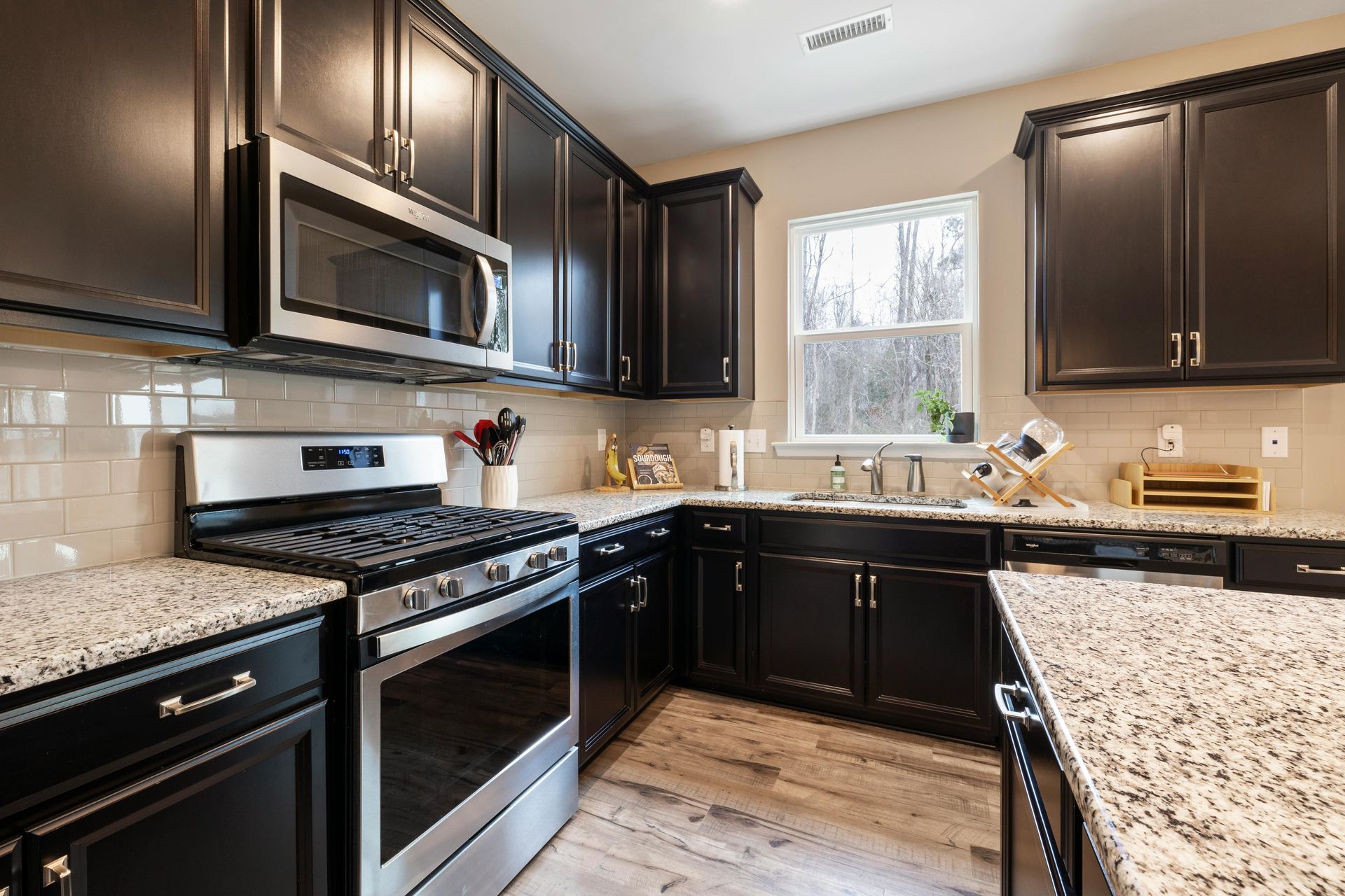 A kitchen featuring dark wood cabinets, granite countertops, stainless steel appliances, and a window over the sink.