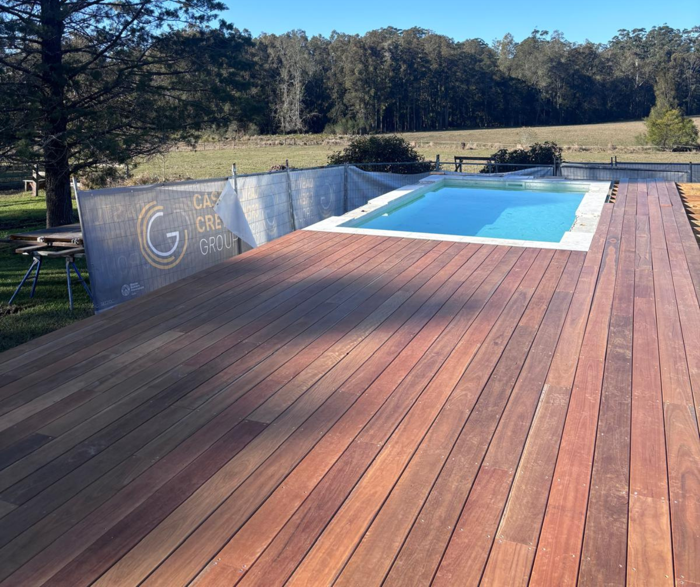Wooden deck with a small blue pool overlooking a grassy field and trees