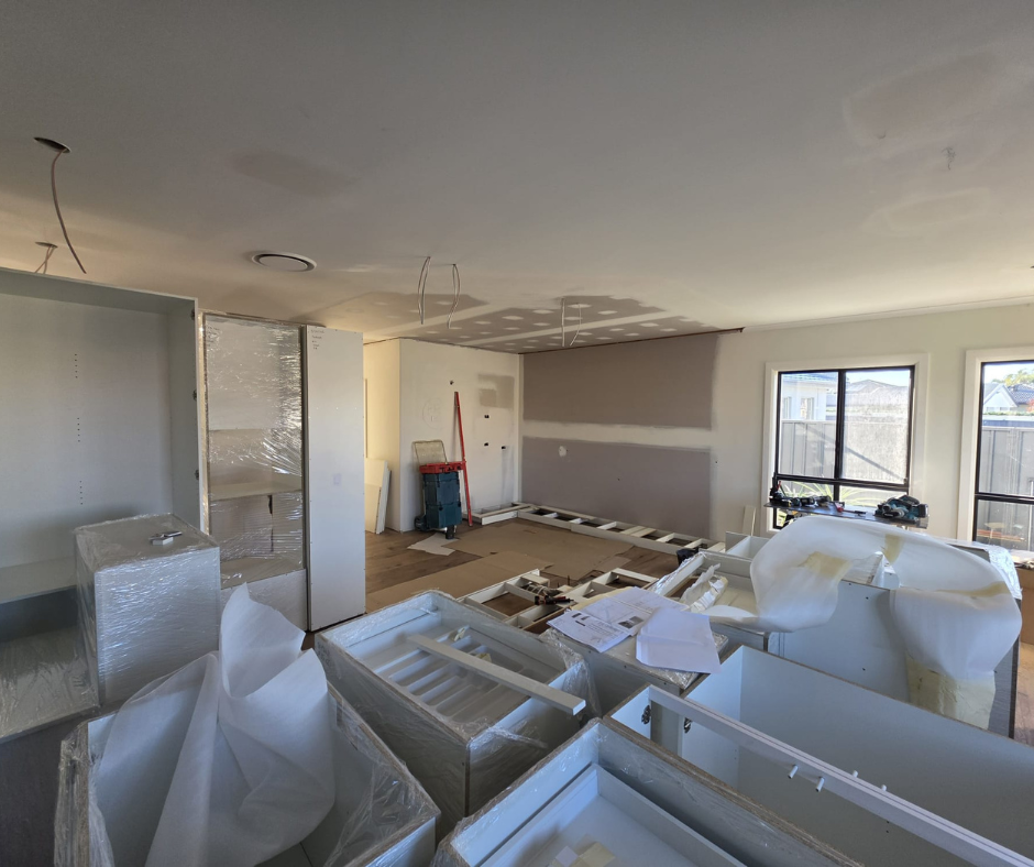 Unfinished living room with covered furniture, cardboard on the floor, and fresh paint on the walls and ceiling.