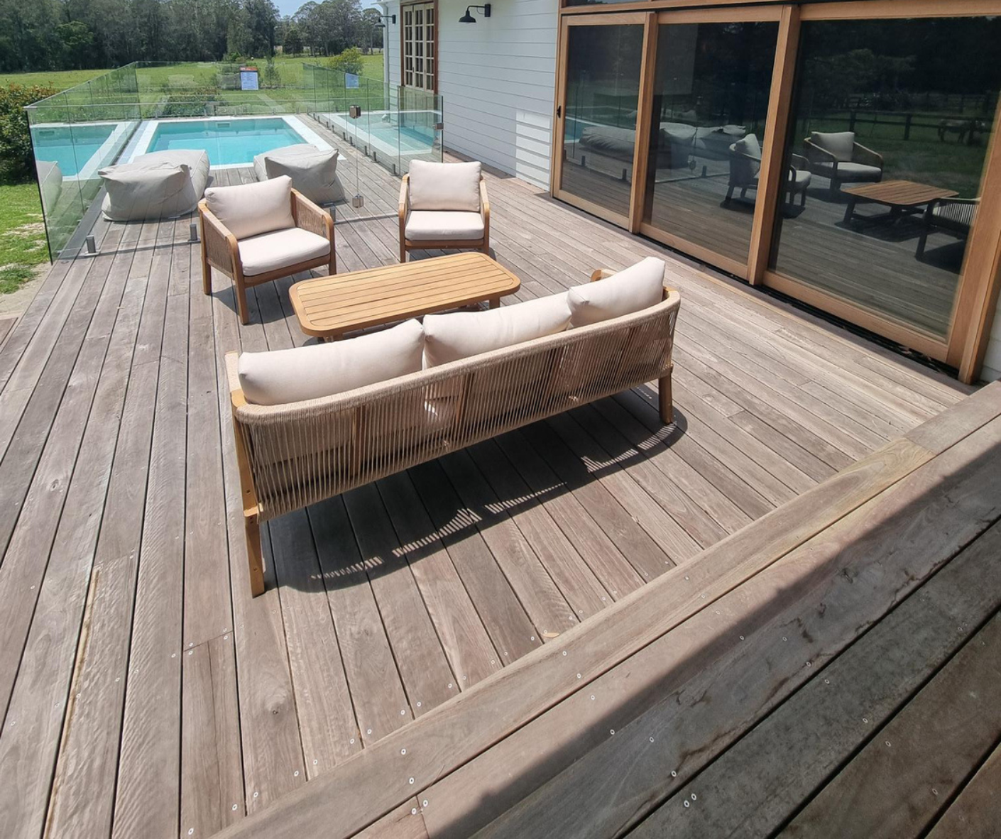 Wooden deck with outdoor sofa and chairs beside a pool, next to a house with sliding glass doors. Wooden deck with outdoor sofa and chairs beside a pool, next to a house with sliding glass doors.