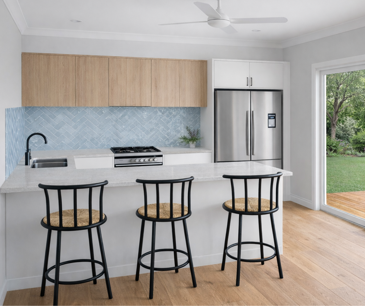 Modern kitchen with white island, three black stools, light wood cabinets, stainless fridge, and patio view.