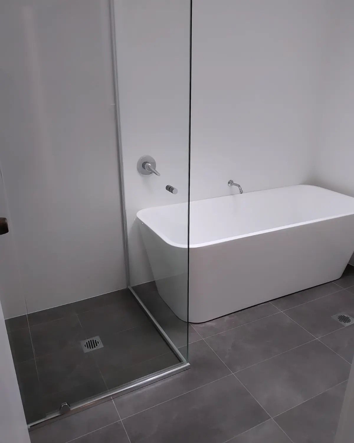 Modern bathroom with a glass shower, a white bathtub, and gray tile floor.