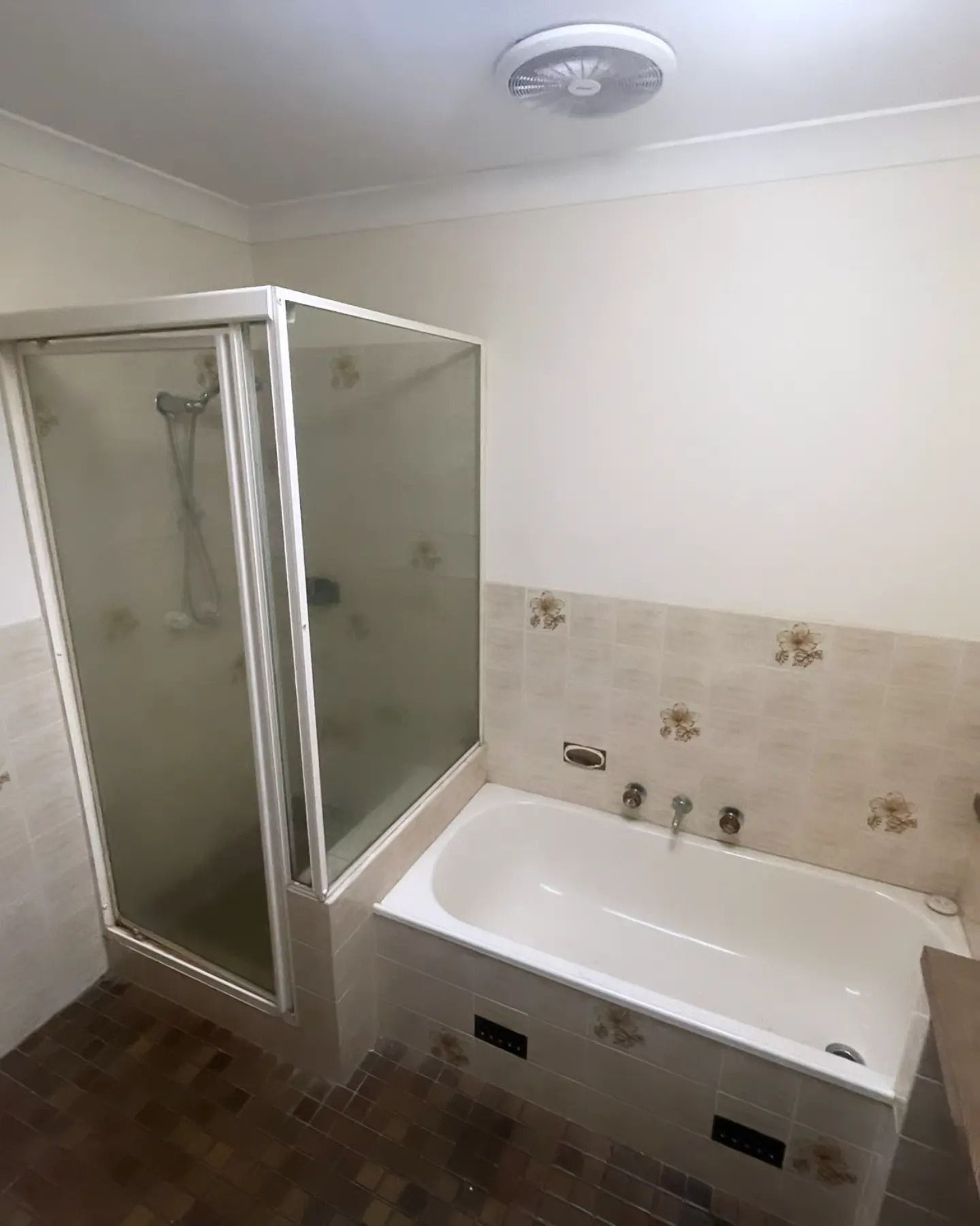 Bathroom with shower stall and bathtub; beige walls, floral tile, and a dark floor.