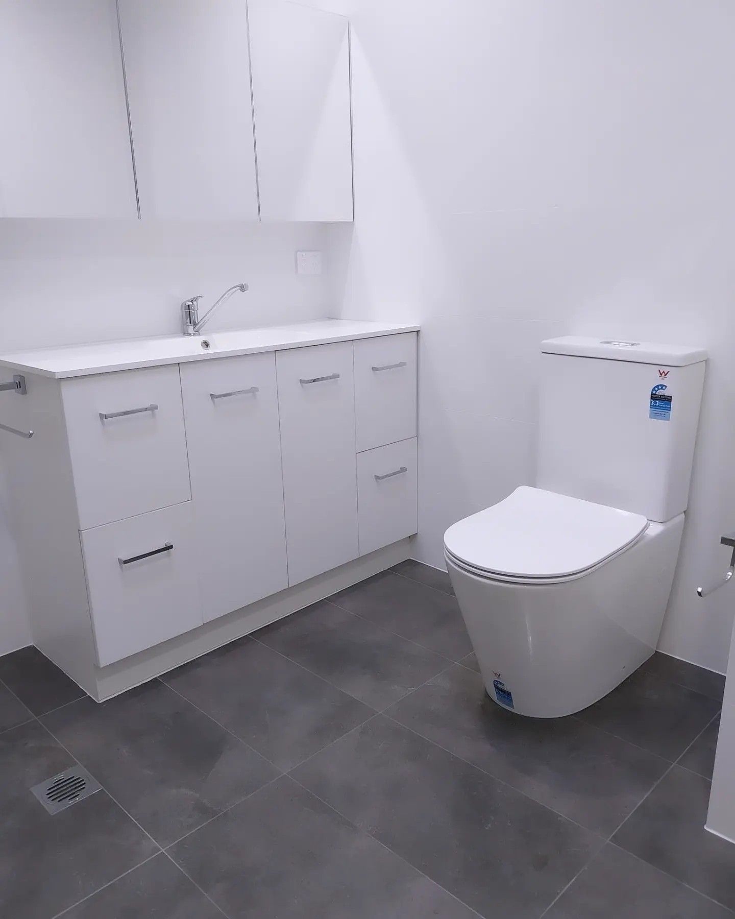 White bathroom with toilet, sink, and cabinets on gray tile floor.