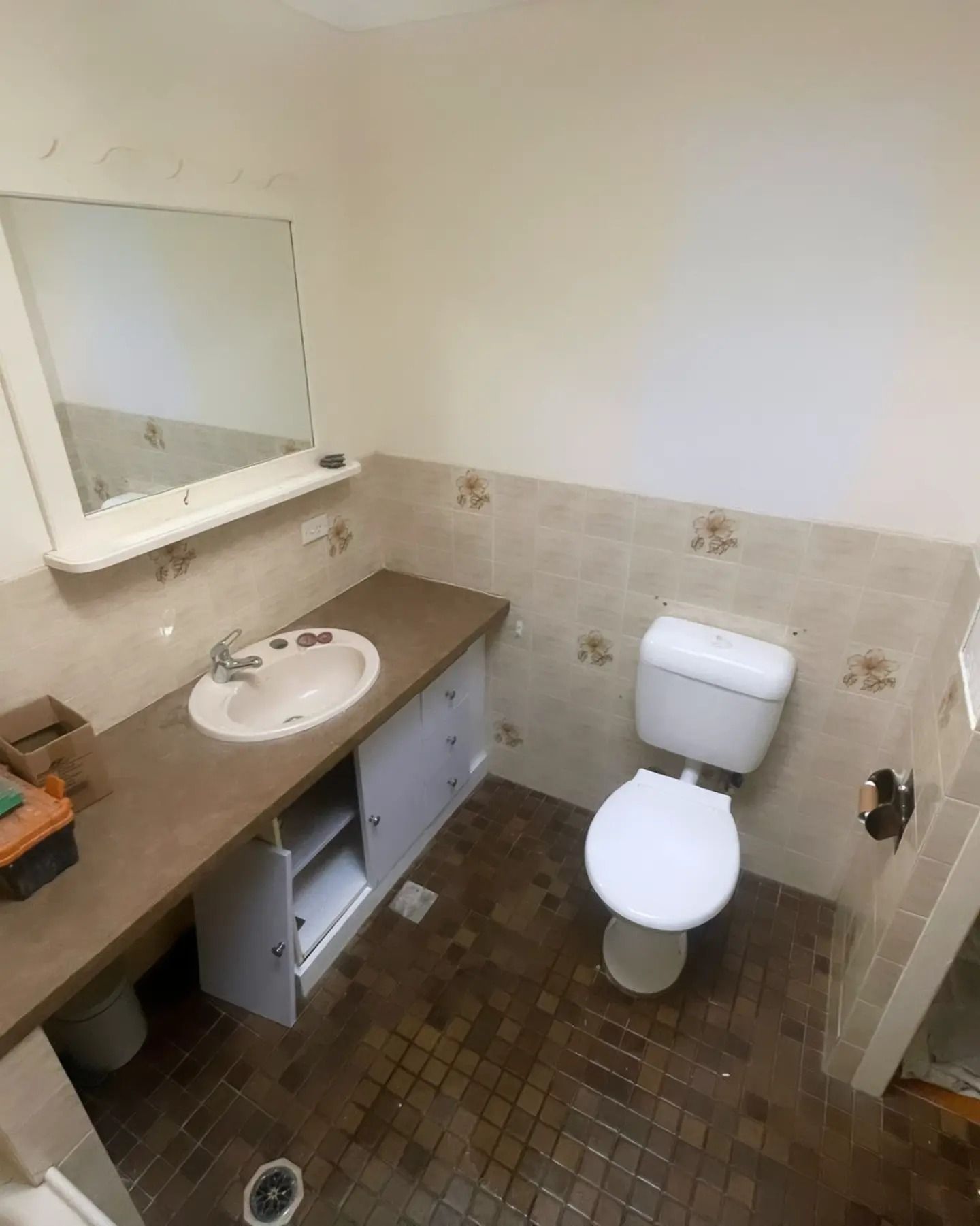 Bathroom with a toilet, sink, mirror, and cabinet. The floor is tiled, and the walls have tile halfway up.