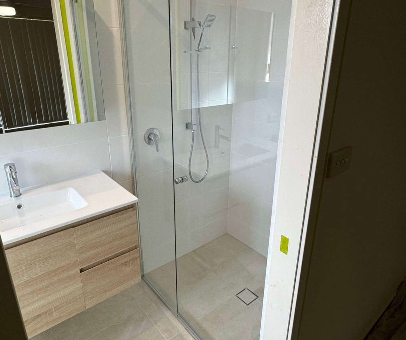 Modern bathroom with glass shower, sink vanity, and mirror, shown in neutral tones.